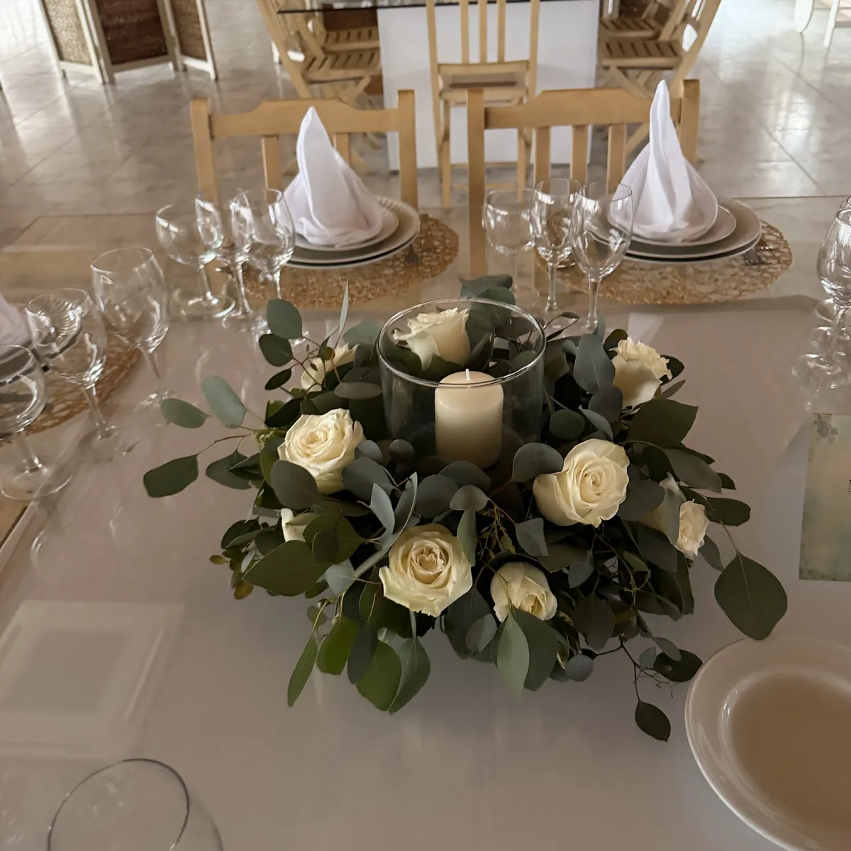 Centro de mesa com rosas brancas, eucalipto e vela num cilindro de vidro